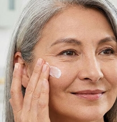Woman applying mature skin skincare cream to her face
